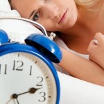 woman in bed staring at clock with insomnia